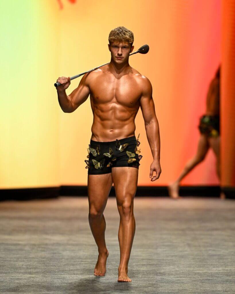 Shirtless male model in swim trunks on the runway