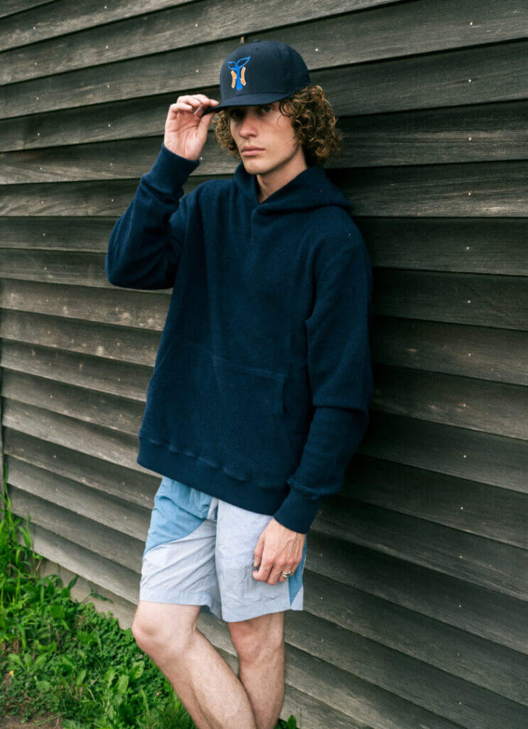 Model in a navy jacket and cap by a wooden wall